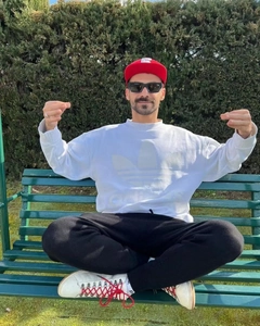 Detail of small rectangular white sunglasses worn with a red baseball cap and hoodie