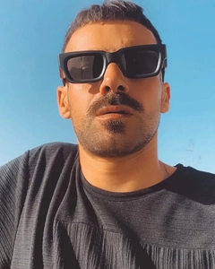 Outdoor low-angle view of a man wearing black wide-frame square sunglasses against a blue sky