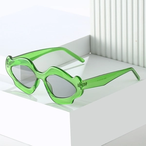 Unique wavy green frame sunglasses with light grey lenses on a white geometric stand