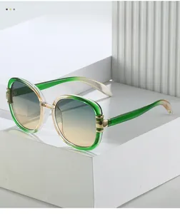 Detailed close-up of oval sunglasses featuring a green gradient frame and gold metal hinge