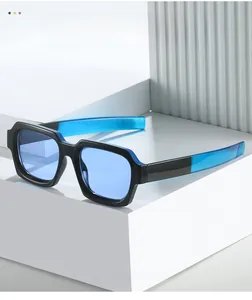 Detail of square black and blue frame sunglasses with light blue lenses on white podium