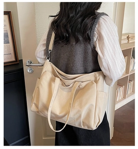 Detail view of a beige canvas tote bag showing side pocket and wide shoulder strap style