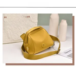 Detail of a ginger yellow oxford fabric crossbody bag with a round metal logo plaque