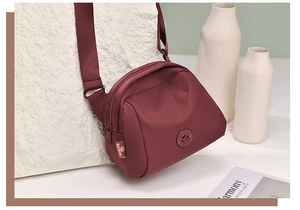 Detail view of burgundy nylon crossbody bag with adjustable strap and shell-shaped design