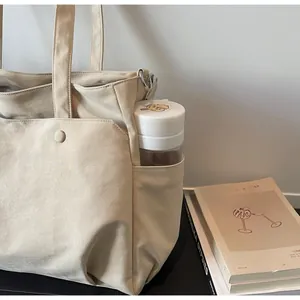 Detail of beige Oxford cloth tote bag side pocket holding a water bottle on a desk