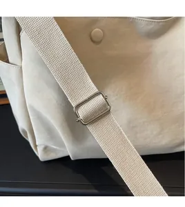 Detail of adjustable woven wide shoulder strap with silver buckle on beige oxford tote bag