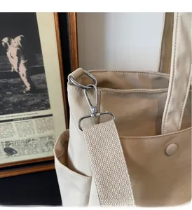 Detailed view of beige canvas tote bag with silver metal swivel hooks and wide woven strap