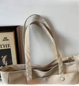 Detail of beige Oxford tote bag showing wide handles, top zipper and front pocket