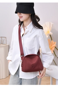 Burgundy nylon shell bag worn as crossbody with wide strap and minimalist logo detail