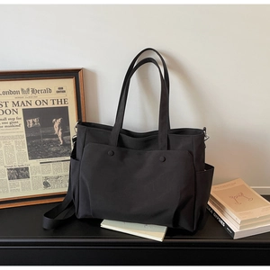 Close-up of a durable black Oxford cloth tote bag with multiple pockets and cross-body strap