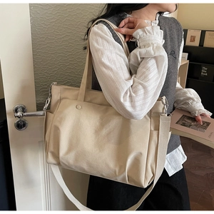 Close-up of beige Oxford tote bag with wide shoulder strap and round buckle pocket detail