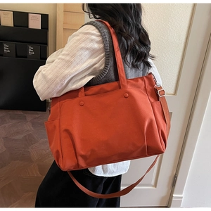Detail of a large brick red Oxford cloth tote bag with shoulder strap and metal hardware