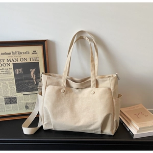 Detail of beige canvas tote bag showing front pockets and adjustable shoulder strap