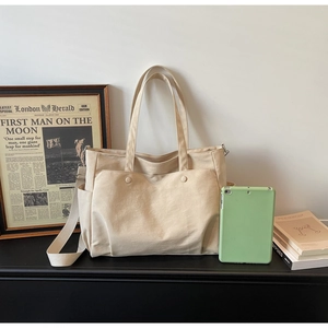 Spacious beige oxford tote bag with dual snap front pockets and adjustable strap shown with books