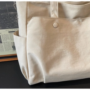 Detail of cream beige nylon tote bag showing side pocket and metal D-ring attachment
