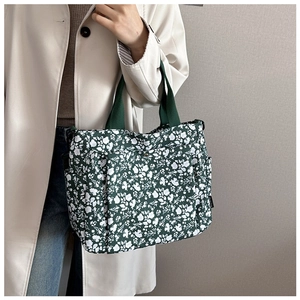 Detail of floral tote bag in dark green featuring white flower patterns and woven handles
