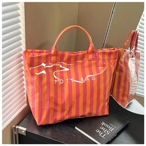 Détail d'un cabas rayé orange et rouge brillant avec lettrage blanc sur surface noire
