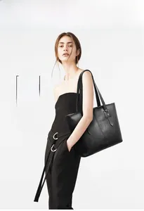 Side view of a large black faux leather tote bag worn by a model in a studio setting