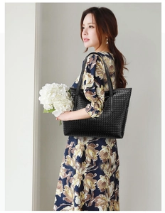 Detailed view of a black woven tote bag styled on a model in a minimalist setting
