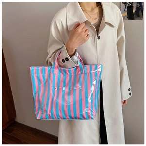 Détail d'un cabas rayé brillant rose et bleu avec texte blanc tenu par un mannequin en trench