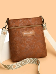Close-up of brown suede crossbody bag featuring paisley embossing and jacquard strap