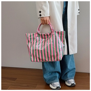 Détail d'un sac cabas à rayures roses et vertes avec finition brillante tenu par un mannequin