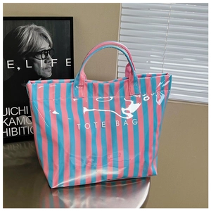 Détail d'un cabas rayé rose et bleu brillant avec l'inscription blanche TOTE BAG
