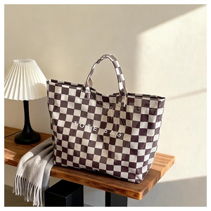 Detail view of brown checkered tote bag with white text on a wooden bench