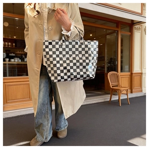 Classic checkered tote bag with white text branding held by a model in street setting