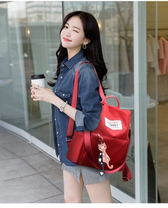 Détail d'un sac à dos rouge en tissu oxford avec accessoire chat en scène extérieure