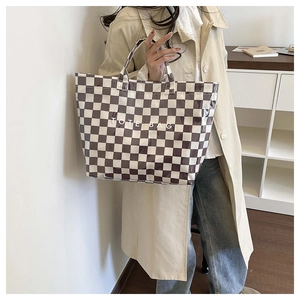 Detailed side view of a black and white checkerboard tote bag held by a model in a modern room