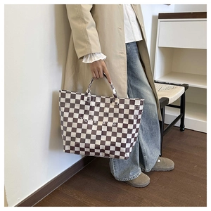 Detail view of checkered tote bag pattern with large white text held by a model