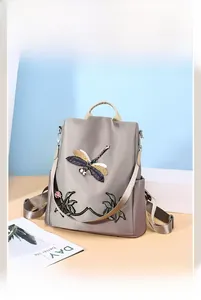 Detail of embroidered dragonfly and flower patterns on grey oxford fabric backpack