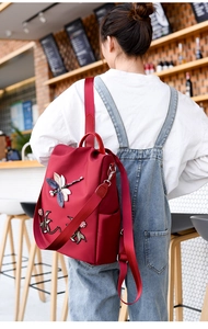 Detail of burgundy oxford backpack featuring 3D embroidered dragonfly and floral patterns
