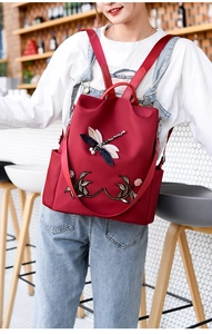 Detail of red oxford backpack featuring 3D dragonfly embroidery and floral patterns