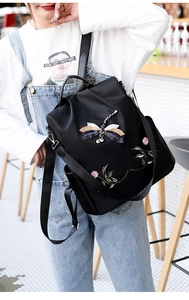 Close-up of a black backpack with intricate 3D dragonfly and floral embroidery detailing