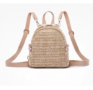 Vista frontale del mini zaino in paglia beige con manico di perle e ciondoli floreali