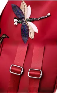 Detail of red backpack featuring a 3D dragonfly embroidery with pearls and metal strap buckles