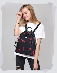 Detail view of lightweight black backpack with red dinosaur prints and bear pendant