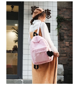 Detailed view of pink plush backpack with a black heart pendant in an outdoor setting