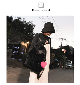 Close-up of black plush backpack featuring a soft texture and a pink heart pom-pom charm