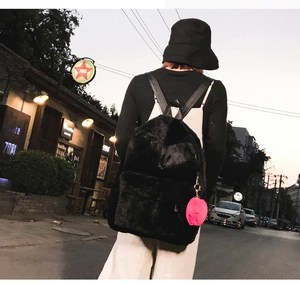 Detail of a black plush backpack featuring a soft faux fur texture and a pink pompom charm