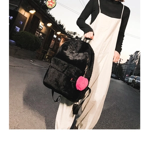 Detail of black plush backpack with pink fur ball charm in casual street setting