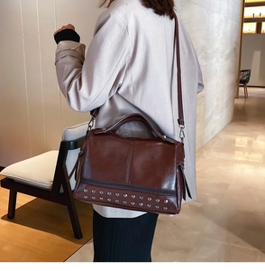 Detail of dark brown glossy leather Boston bag with silver rivets and metal shoulder strap