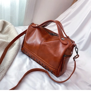Detail view of caramel brown Boston bag showing silver rivets and soft PU leather texture