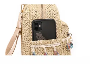 Detail of the woven straw backpack side pocket holding a smartphone with tassel charm