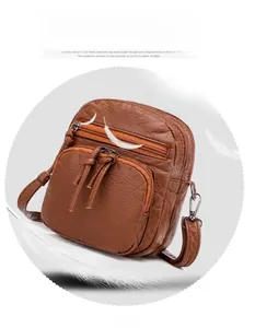 Macro detail of brown soft leather crossbody bag showing three multi-layered zipper pockets