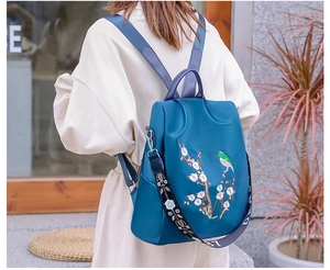Dettaglio di ricamo con gazza e fiori di prugno su uno zaino in nylon blu