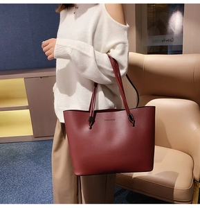 Deep red matte leather tote bag shown on a model in a minimalist indoor setting