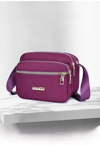 Detail view of purple nylon crossbody bag with multiple zippers and golden logo plate